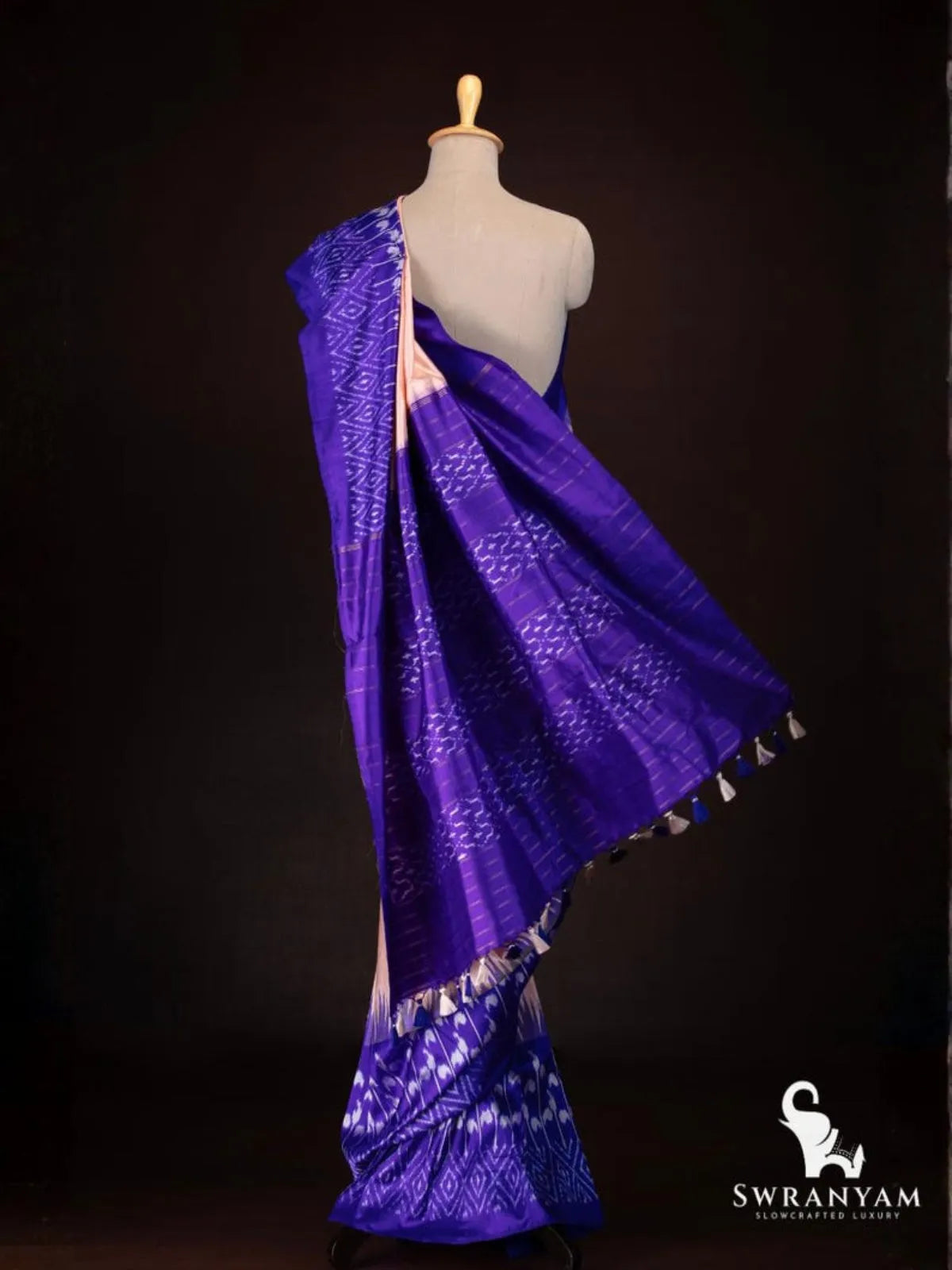 Back view of royal purple and peach tussar silk ikat saree showing purple pallu with ikat bands, woven stripes and tassels