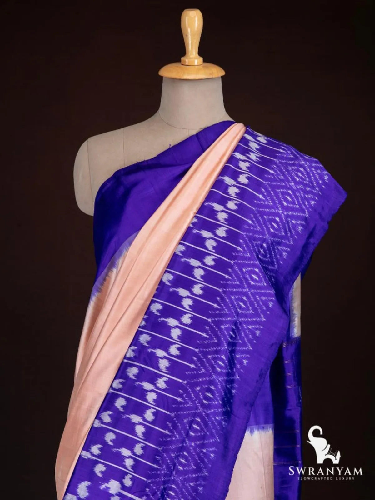 Close-up of royal purple ikat border with white paisley and diamond motifs on peach tussar silk saree shoulder drape