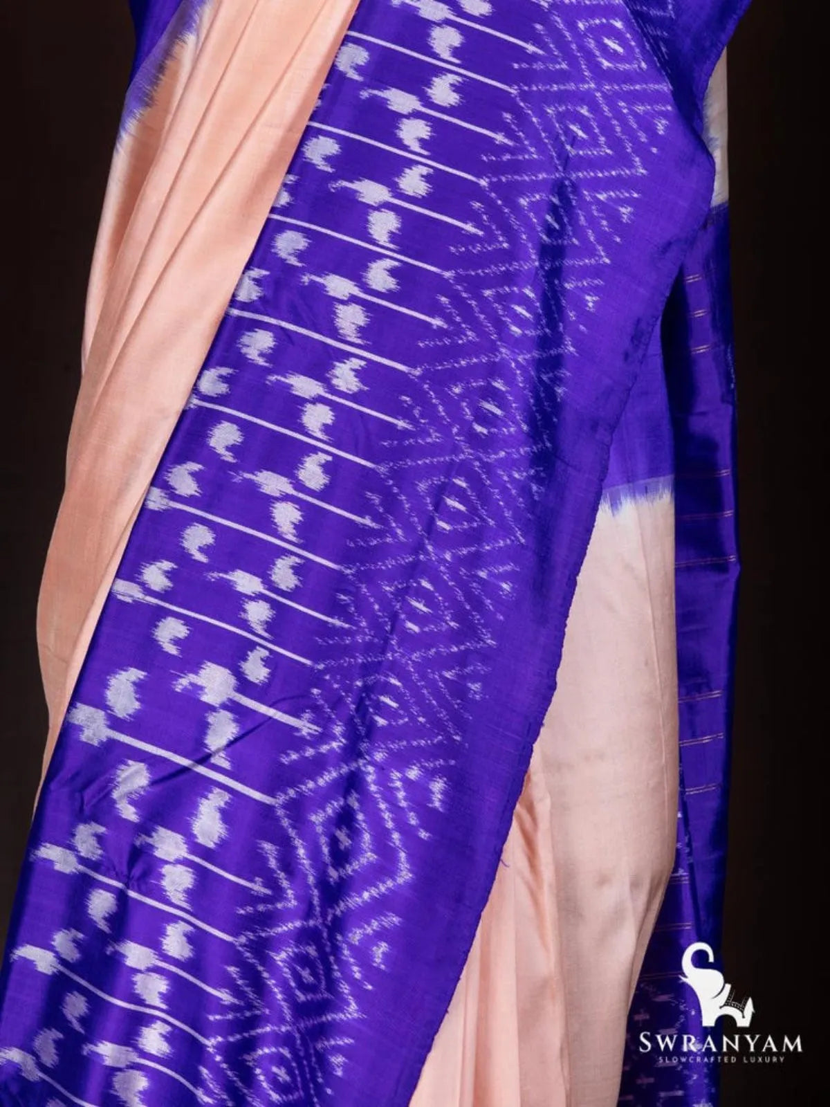 Close-up of white paisley ikat motifs on royal purple border beside soft peach tussar silk body of the saree
