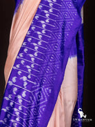 Close-up of white paisley ikat motifs on royal purple border beside soft peach tussar silk body of the saree