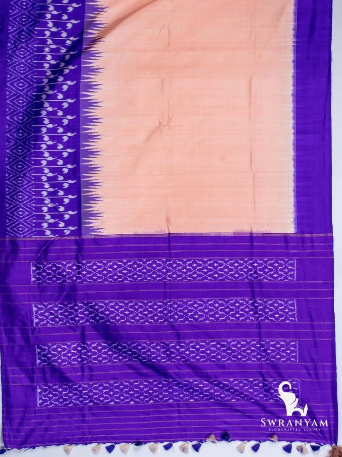 Peach tussar silk ikat saree spread flat showing royal purple temple border, ikat panels and purple pallu with tassels