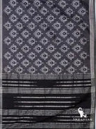 Charcoal grey Pochampally ikat cotton silk saree spread flat showing white ikat motifs and black pallu with silver stripes