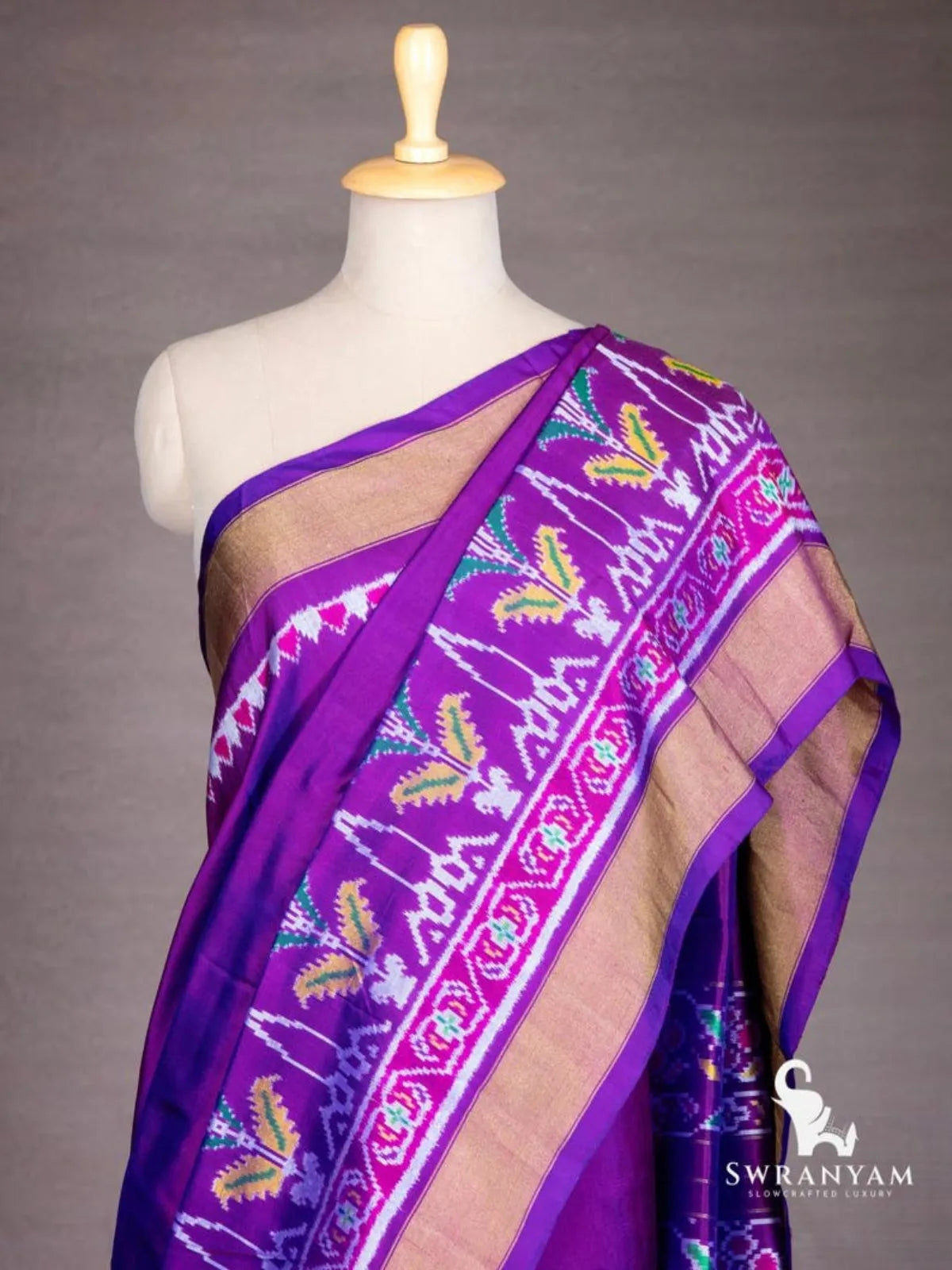 Close-up of royal purple ikat silk saree shoulder drape with pink ikat border, leaf motifs and wide gold zari border