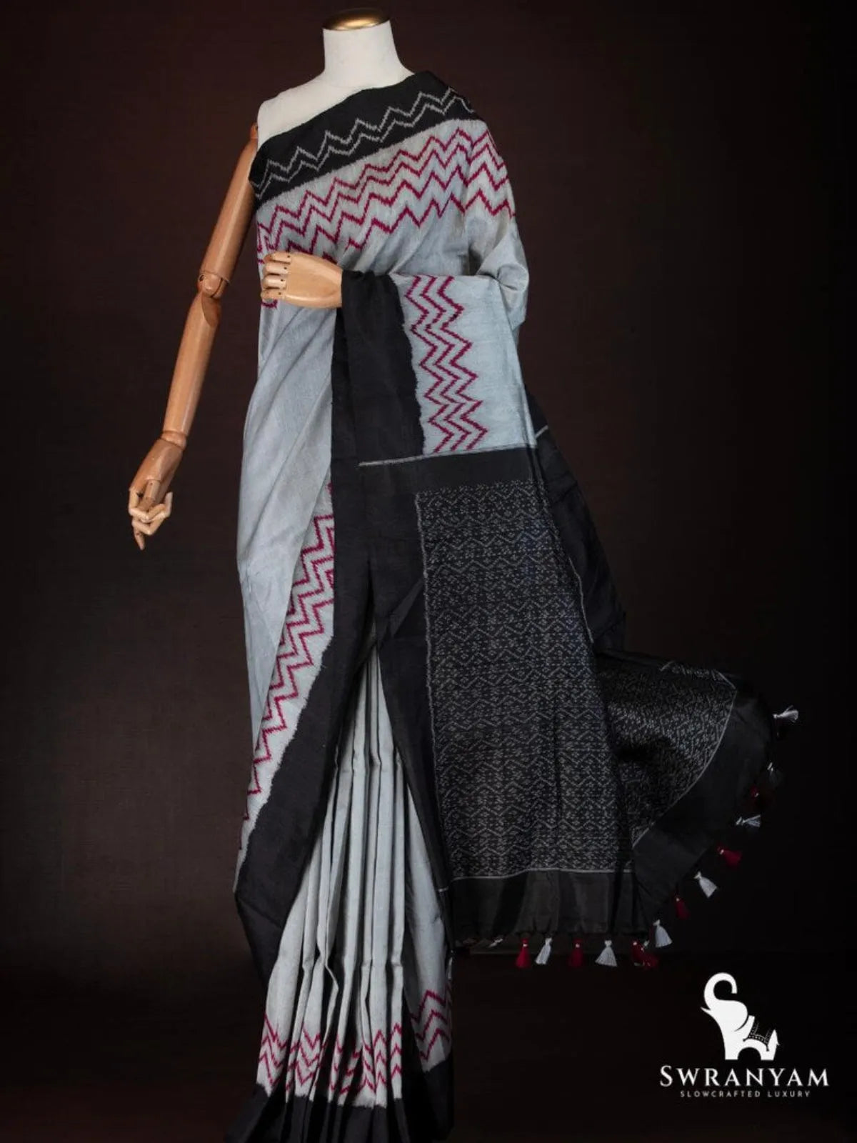 Black ikat pallu with white woven motifs and grey and red tassels flowing on charcoal grey tussar silk saree