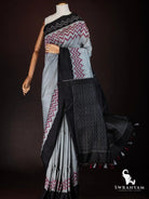Black ikat pallu with white woven motifs and grey and red tassels flowing on charcoal grey tussar silk saree