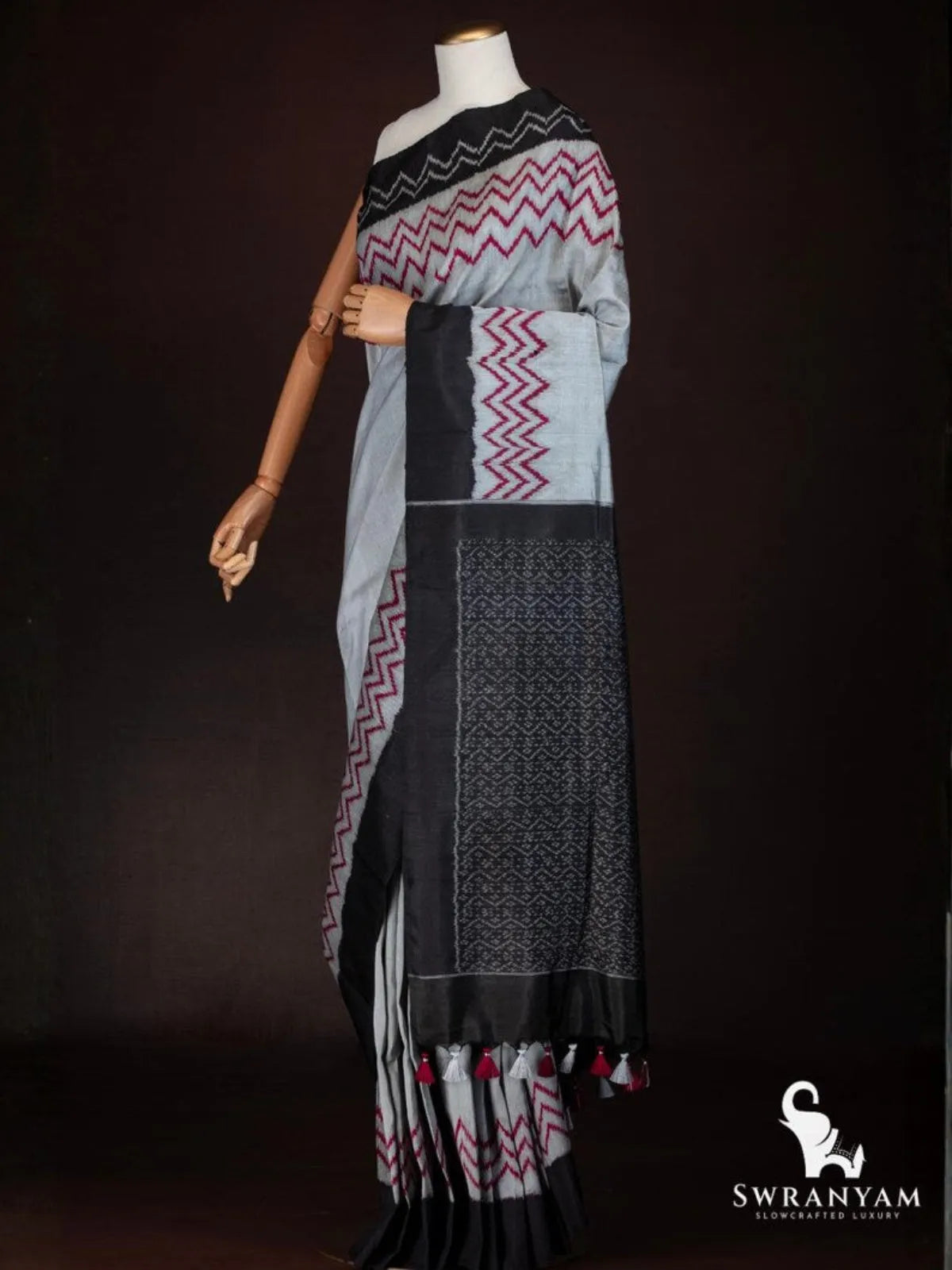 Charcoal grey tussar silk saree pallu in black with fine white ikat motifs and red and grey tassels, side view
