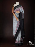 Side view of charcoal grey tussar silk saree with red zigzag ikat border, black pallu and tassels on mannequin