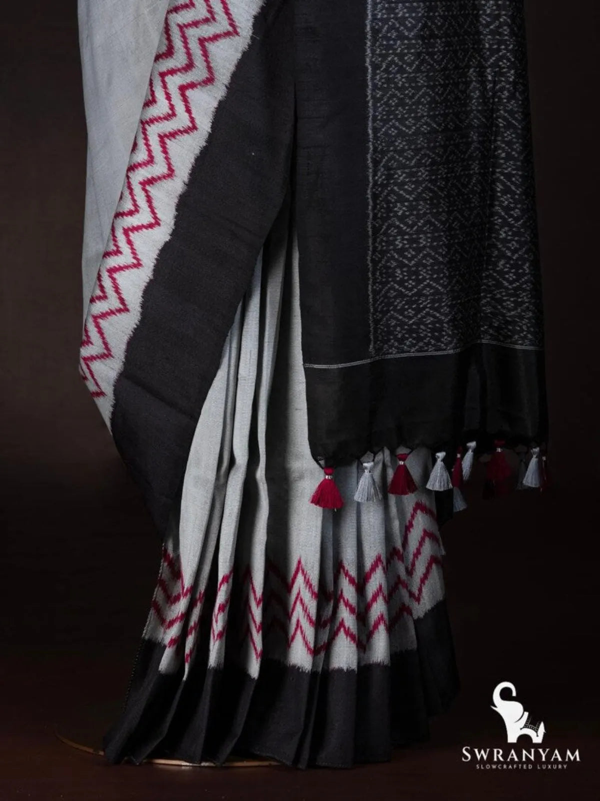 Close-up of tussar silk ikat saree pleats with red zigzag hem, black border and red and grey tassels