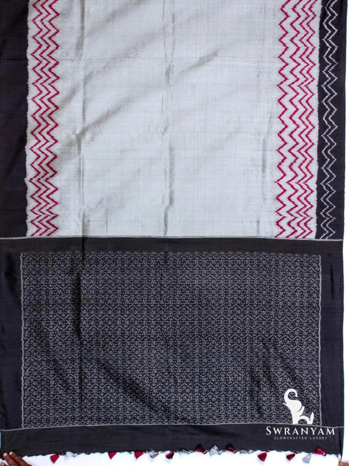 Charcoal grey tussar silk ikat saree spread flat showing red zigzag borders, black border and black patterned pallu