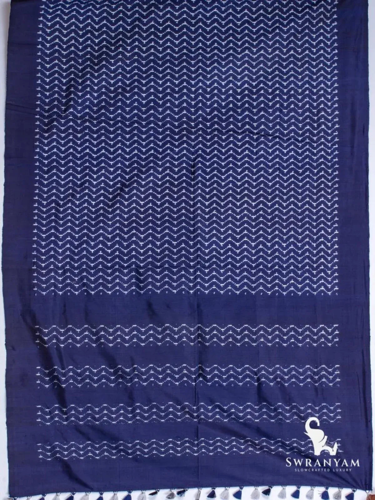 Indigo blue Pochampally ikat silk saree spread flat showing white chevron ikat body, solid border and pallu with tassels