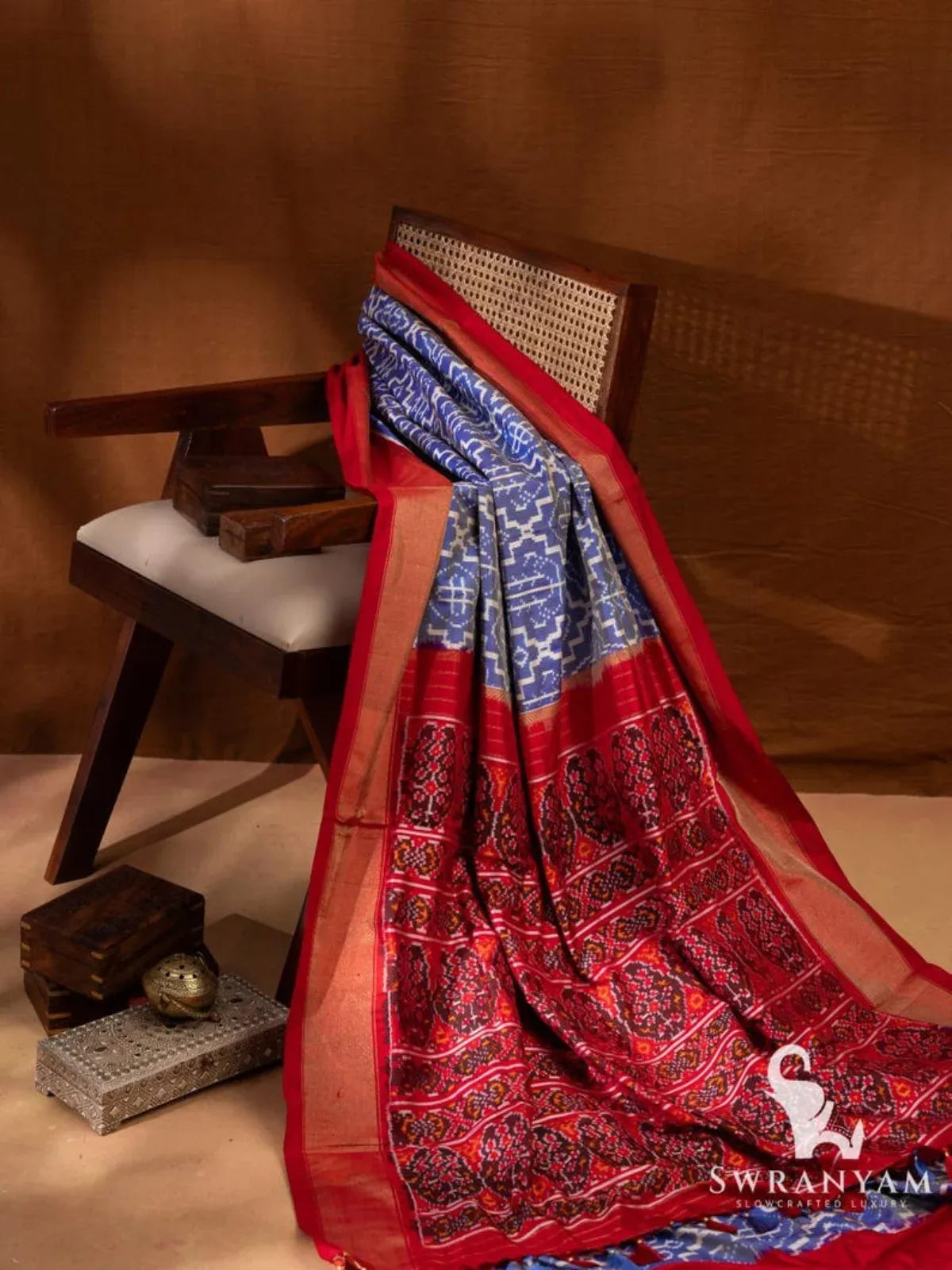 Blue and red Pochampally ikat silk saree draped on wooden chair showing ikat body, red pallu and zari temple border