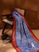 Blue handwoven ikat silk saree with geometric motifs and red zari temple border, full length view on wooden chair
