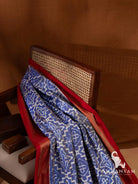 Pleated blue Pochampally ikat silk saree with white geometric motifs draped over a cane back chair, red border visible
