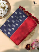 Folded navy blue Pochampally ikat silk saree with red border and red tassels styled with flowers on a woven mat