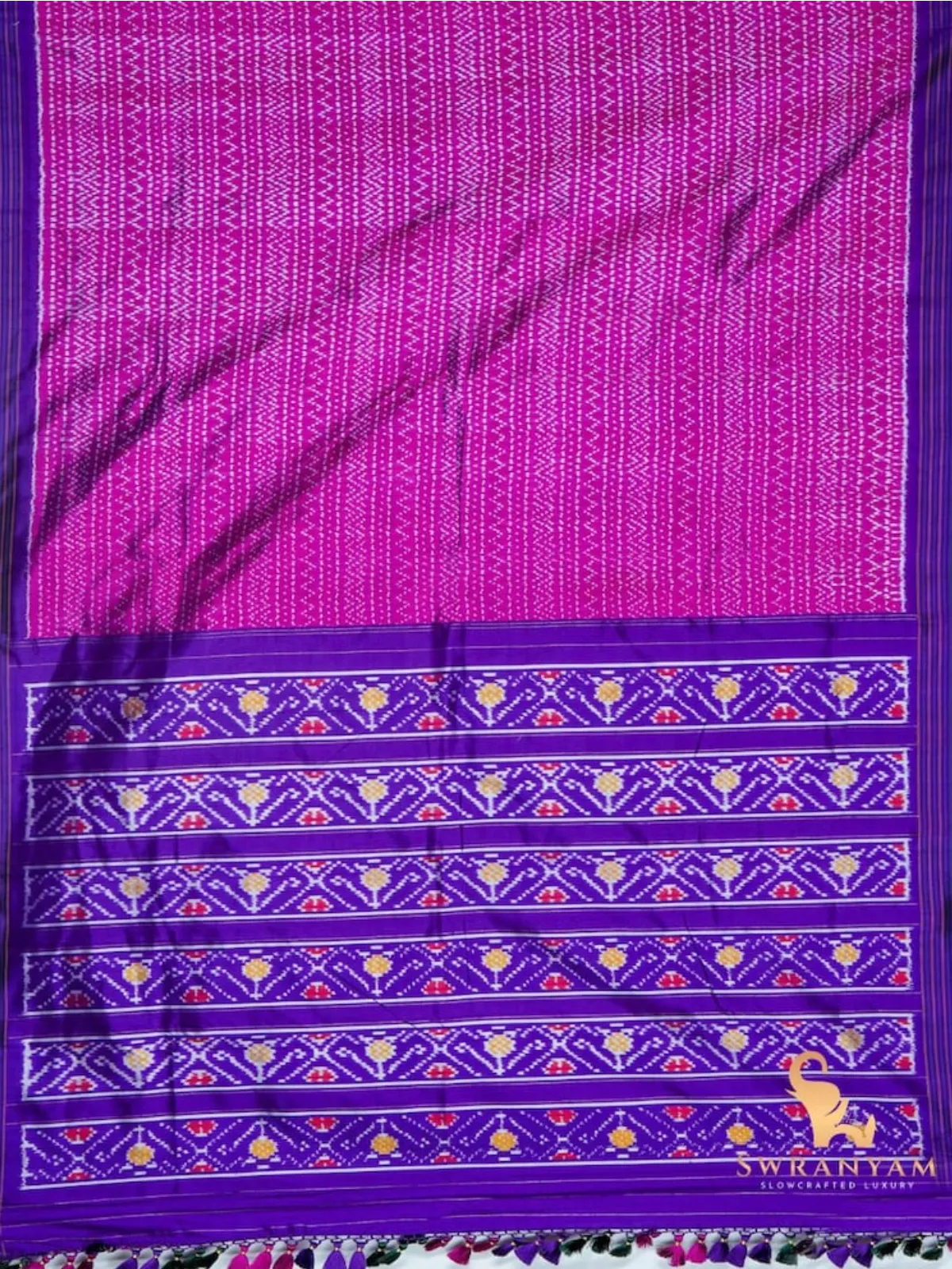 Flat lay of pink Pochampally ikat silk saree with zigzag body and purple pallu bands of traditional ikat motifs
