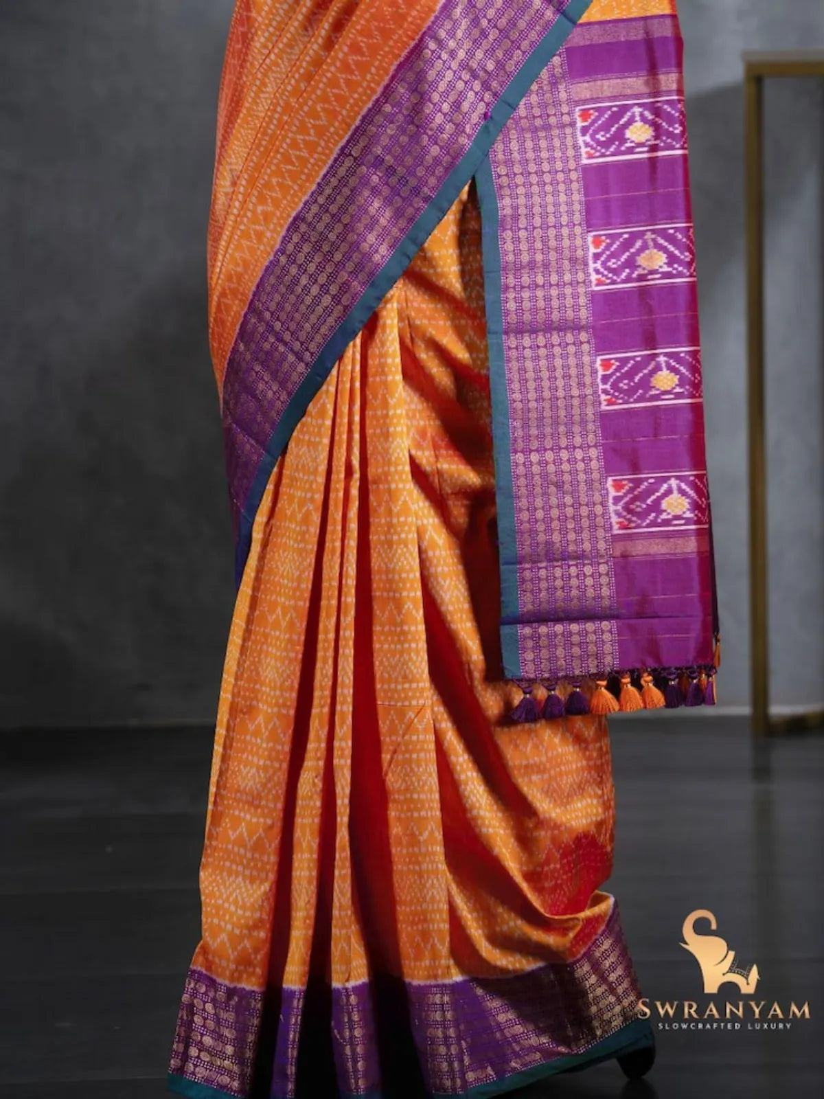 Pleats of orange ikat silk saree with purple border and tasselled pallu showing traditional ikat motifs